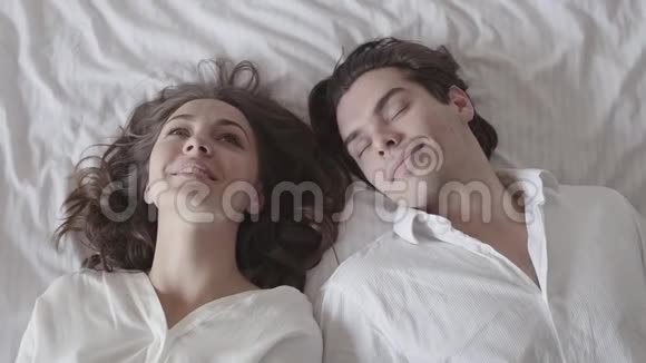 可爱的男人和女人落在床上用爱看着对方年轻夫妇躺在床上投标视频的预览图