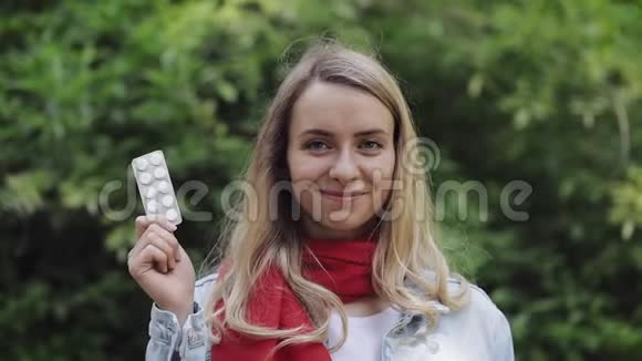 美丽微笑的女人戴着红色围巾手里拿着药丸站在城里的画像视频的预览图