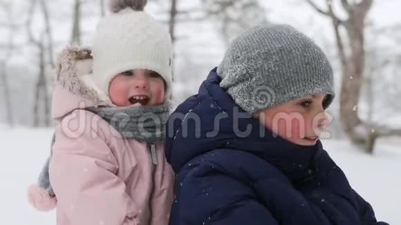 女儿帮助母亲在降雪时和儿子拉雪橇幸福的家庭在下雪的冬天滑雪可爱的小女孩视频的预览图