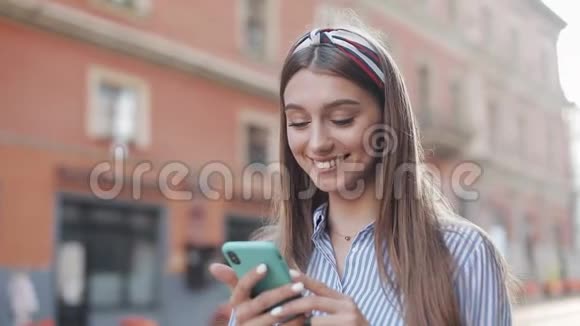 一个穿着蓝白相间条纹连衣裙的可爱女人站在老城街上用智能手机上的app美丽的视频的预览图