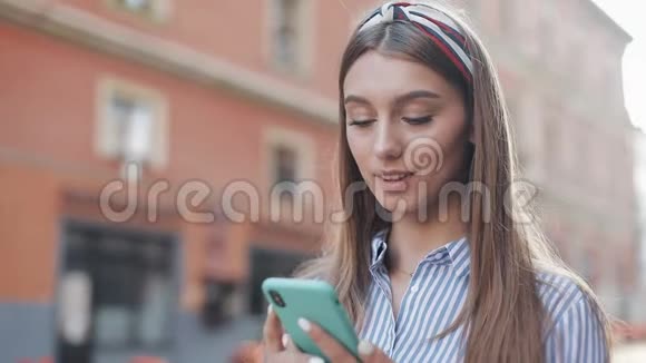 一个穿着蓝白相间条纹连衣裙的可爱女人站在老城街上用智能手机上的app美丽的视频的预览图