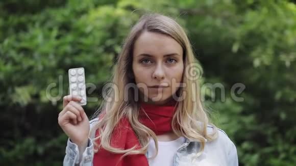 美丽微笑的女人戴着红色围巾手里拿着药丸站在城里的画像视频的预览图