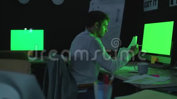 年轻的商人在夜间办公室用绿色显示器做电脑工作视频的预览图