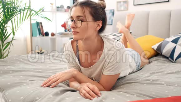 一张年轻迷人的高加索女人戴眼镜的肖像早上躺在卧室的床上视频的预览图