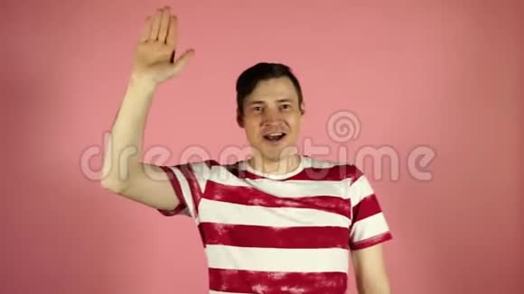 一个穿着粉红色背景条纹t恤的男人一个欢快的年轻人挥舞着手的肖像视频的预览图