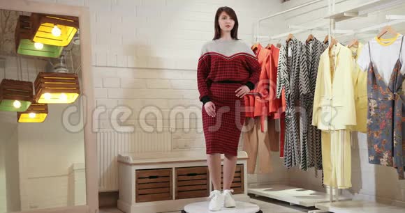 一个漂亮的女孩在转盘上绕着她的轴线旋转展示服装的模型穿红色和灰色毛衣的模特4k视频的预览图