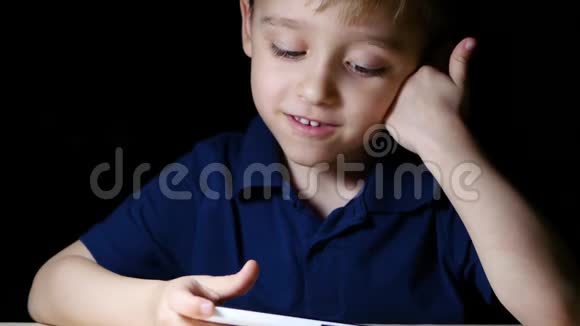 一个孩子带着一幅漫画晚上在家里用智能手机看着一幅漫画微笑着特写镜头视频的预览图