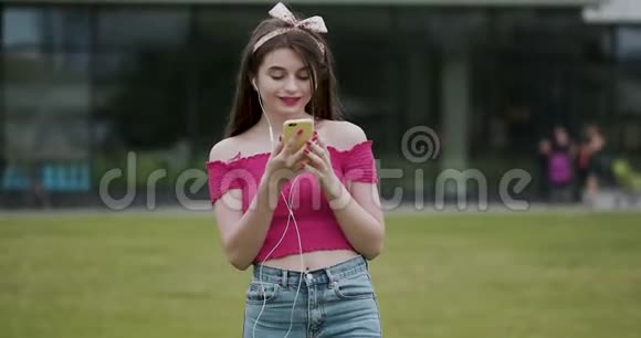 吸引人的年轻女孩在城市街道背景听音乐耳机穿粉色上衣的女人视频的预览图