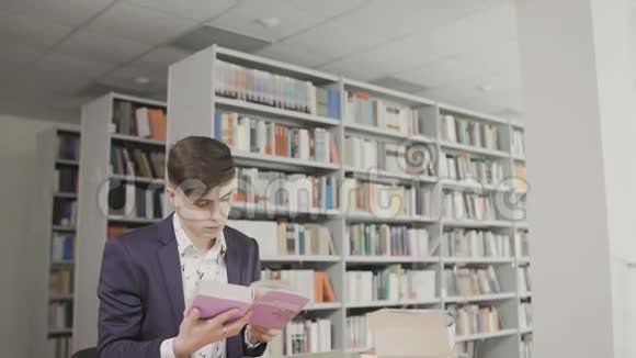 年轻的男学生在图书馆看书在书架背景上穿西装看书的人视频的预览图