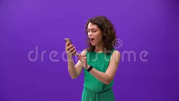 Curly女孩用一个紫色背景的新手机玩游戏视频的预览图