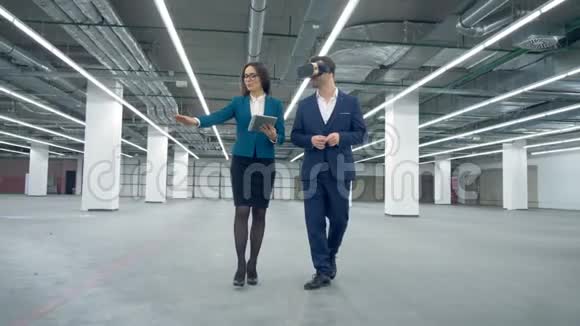 女特工正在向一个戴着虚拟现实眼镜的男人展示空荡荡的办公场所视频的预览图