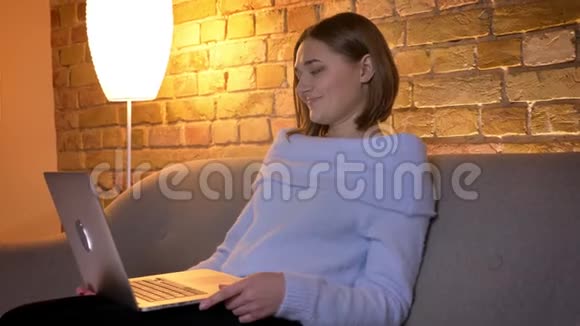 坐在沙发上在舒适的家中放松的年轻漂亮女性在笔记本电脑上的特写镜头视频的预览图