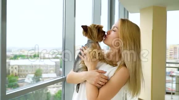 一个快乐的金发女人手上抱着一只毛茸茸的小狗亲吻它视频的预览图
