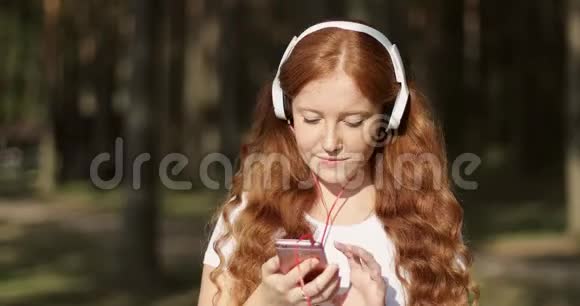 年轻快乐女人的肖像红色卷发享受户外音乐视频的预览图