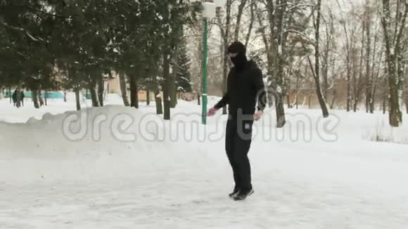 年轻人戴着面具穿着黑色运动服在白雪覆盖的公园里做运动跳绳视频的预览图