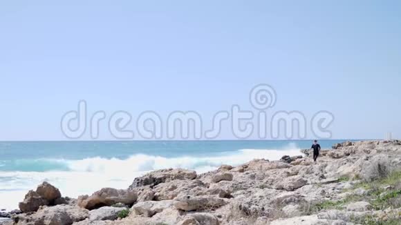 白人运动员穿着黑色的衣服在岩石海滩上跑过岩石视频的预览图