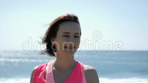 年轻漂亮的白种人女子肖像微笑着看着站在海滩上的摄像机视频的预览图