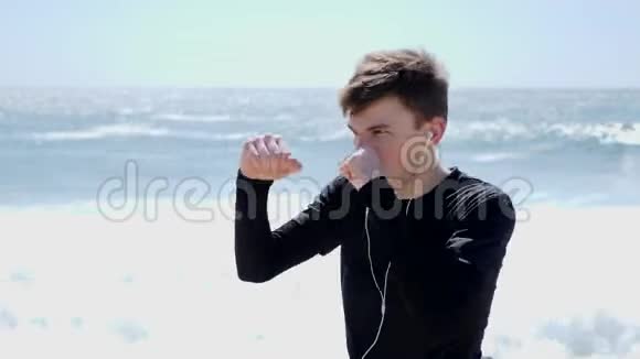 年轻的白种人运动员戴着耳机在空中打拳沙滩拳击练习视频的预览图