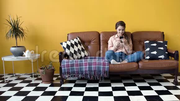 漂亮的年轻女人坐在沙发上打电话库存录像有魅力的女人在电话里翻新闻视频的预览图