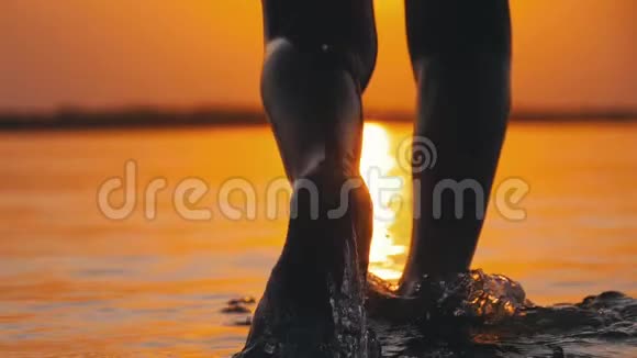 日落时男孩的腿的剪影跑到水里并产生飞溅慢动作视频的预览图