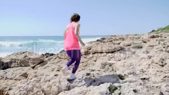 年轻的运动女孩穿着粉红色的衣服在岩石小径上奔跑后射视频的预览图
