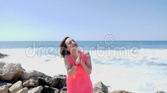 年轻美丽的快乐女孩拍手跳在一个岩石海滩上海浪和水溅风和日丽的日子视频的预览图