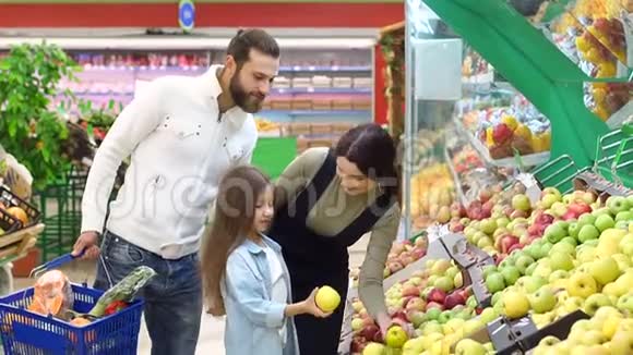 有一个小女儿的年轻父母在一家大型超市里选择新鲜的苹果视频的预览图