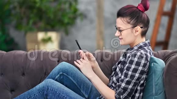 微笑时髦的年轻女性用智能手机聊天坐在家里的沙发上中档视频的预览图