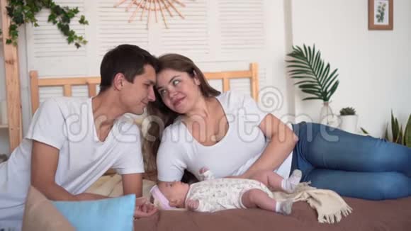 家人在床上微笑爸爸和妈妈在那里看触摸和交谈他们的小女儿爸爸吻妈妈的额头视频的预览图