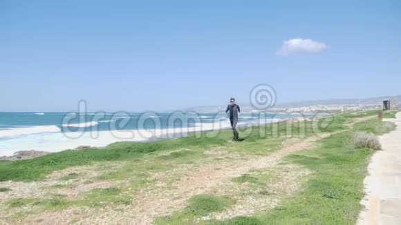 年轻强壮的白种人穿着黑色的衣服和太阳镜在海滩上奔跑小径沿着大海视频的预览图