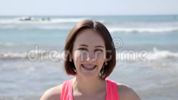 年轻漂亮的女孩带着牙套在海滩上微笑波浪般的海洋视频的预览图