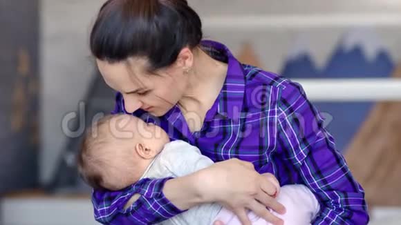 中度特写临时照顾的母亲微笑着亲吻双手上的熟睡婴儿视频的预览图