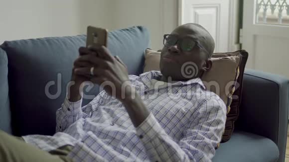 年轻的非裔美国人在沙发上用智能手机视频的预览图