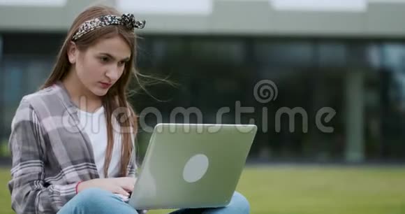 女性在户外坐在绿色的新鲜草坪上在笔记本电脑上打字自由职业者博客作者记者视频的预览图