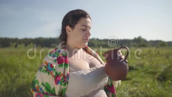 可爱的超重女人喜欢从绿色的夏田上的土罐喝新鲜牛奶美丽的风景视频的预览图