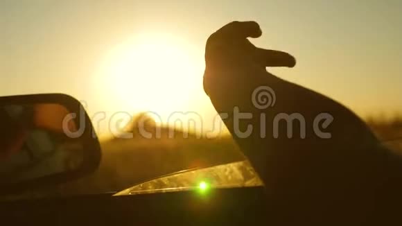 女孩手挥动太阳乘车旅行司机的手正在玩太阳从车窗对着美丽的日落视频的预览图