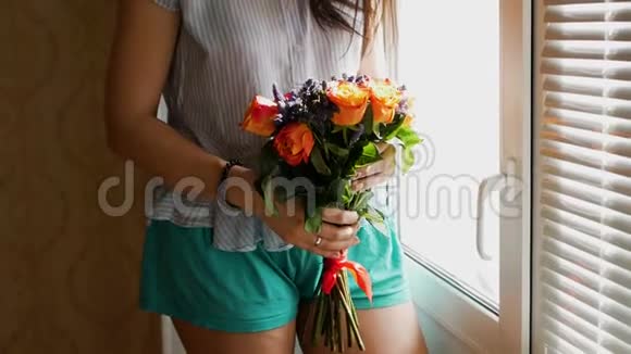 一个漂亮的女孩把一束花送到鼻子上闻着它们站在窗前中型射击视频的预览图