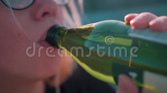 一个从绿色玻璃瓶中喝水的女孩的电影特写冷静的计划慢动作视频的预览图