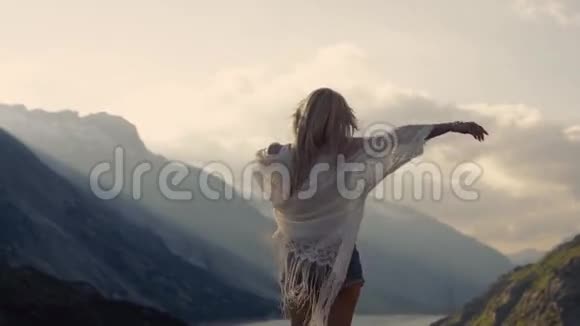穿着时髦牛仔裤短裤的女孩站在山顶上朝太阳走去视频的预览图