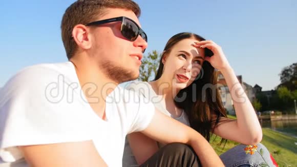 浪漫的夫妇笑着坐在池塘边的绿草上夫妻信任爱和幸福的概念中弹视频的预览图