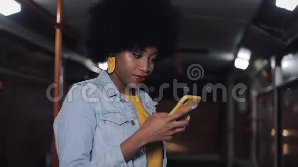 吸引人的是年轻的非裔美国妇女在公共交通中使用智能手机晚上城市灯光背景视频的预览图