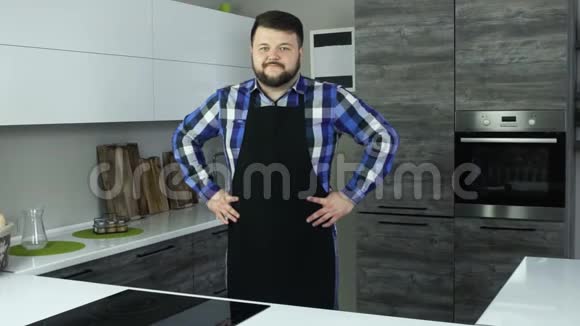 一个穿着围裙的胖子站在厨房的中央双手放在一边微笑一个穿着围裙的胖子视频的预览图