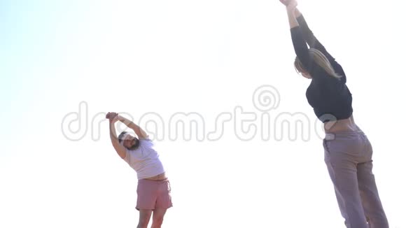 一个留着胡子的白种人和一个在沙质海岸附近的河边做瑜伽的女孩动态瑜伽和视频的预览图