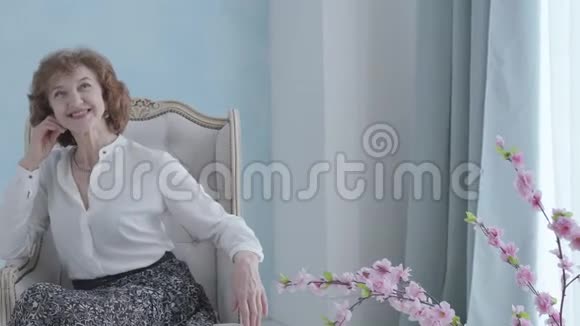 肖像美丽可爱优雅成熟的女人穿着白色衬衫坐在扶手椅上微笑无法辨认的人视频的预览图
