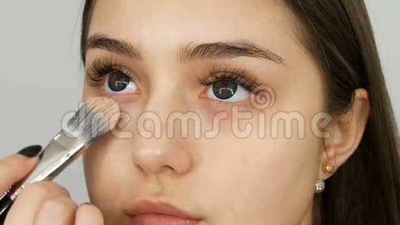 化妆师做化妆女孩模特在美容店里用特殊的刷子将遮瑕粉涂在女孩脸上视频的预览图
