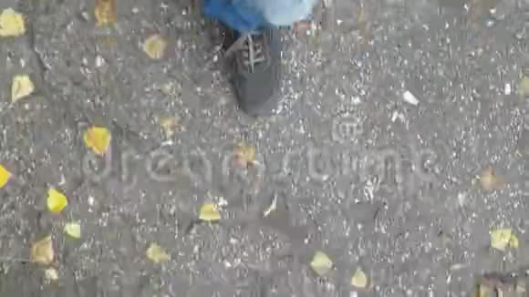 在秋天的一天一个穿着牛仔裤和鞋子的男人走在潮湿的沥青和水坑上Pontofview视频的预览图
