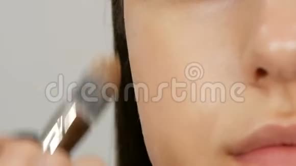化妆师做化妆女孩模特在美容店里用特殊的刷子将遮瑕粉涂在女孩脸上视频的预览图