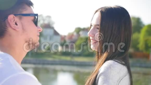 在池塘附近的绿色夏季公园里的浪漫情侣一个男人调情逗一个女孩开心一起快乐太阳关门视频的预览图