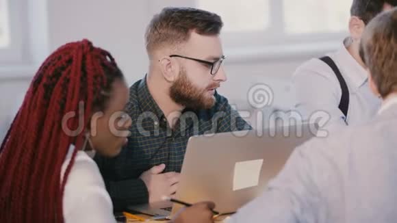 年轻认真专注的高加索软件开发人员在现代笔记本电脑上工作在多民族的团队会议上倾听视频的预览图