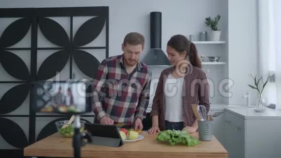 健康饮食博客女性和男性博客写手在厨房里用蔬菜和蔬菜准备有用的食物同时拍照视频的预览图